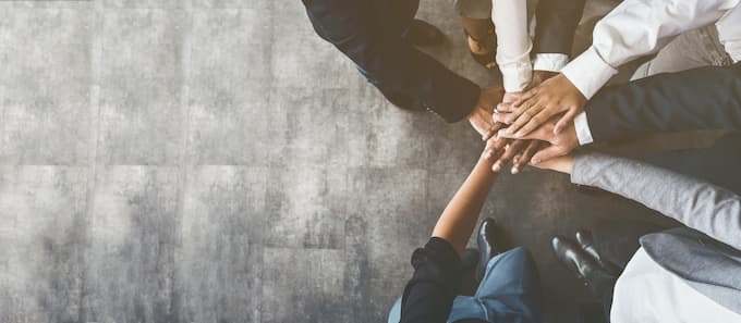 Karriere-Jobs-bei-EWE Geschäftliche Zusammenarbeit: Menschen stehen im Kreis und legen ihre Hände zusammen, um Einheit und Teamgeist zu zeigen.
